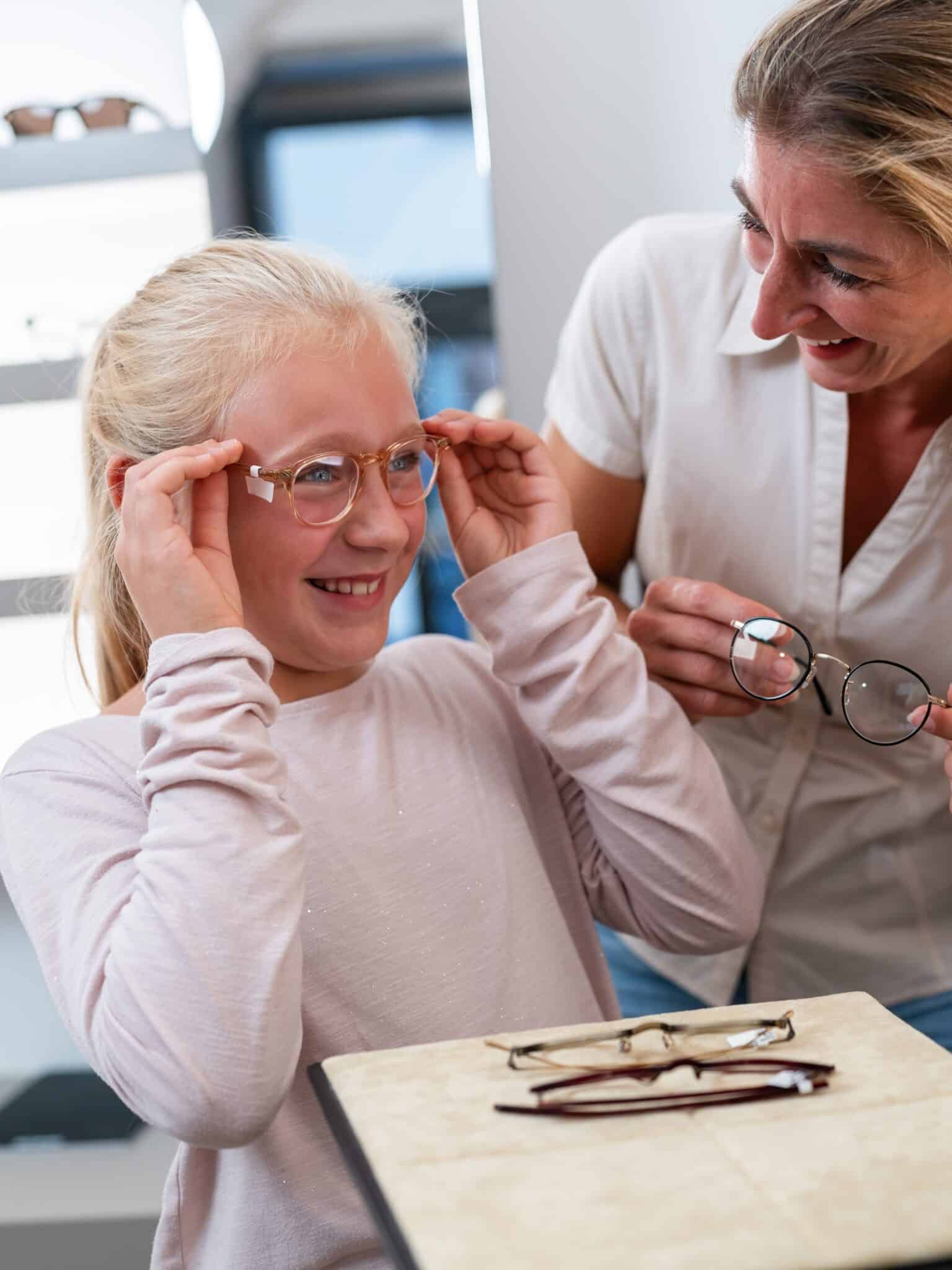 shutterstock_2401210323 A young girl is trying on glasses and smiling.
